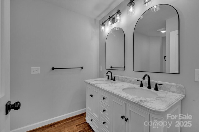 bathroom featuring a sink, baseboards, wood finished floors, and double vanity