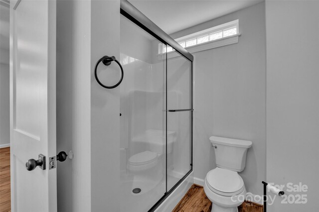 full bathroom featuring a stall shower, toilet, baseboards, and wood finished floors