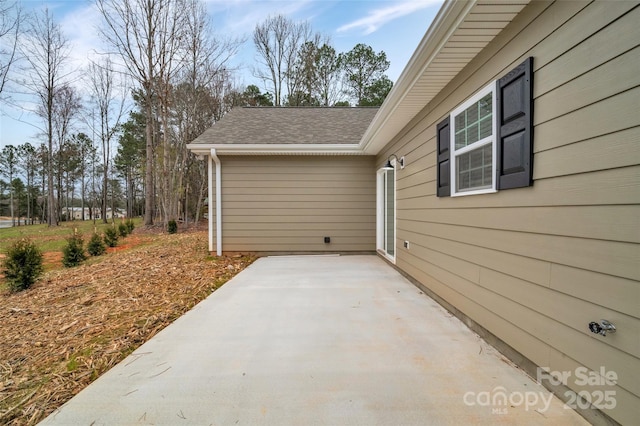 view of side of home with a shingled roof and a patio