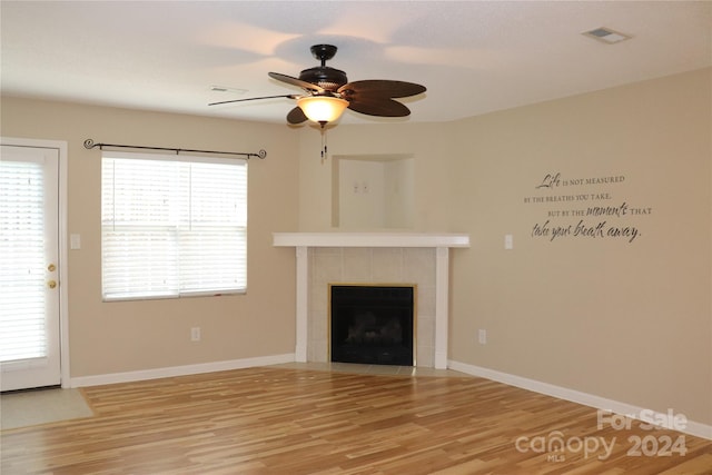 unfurnished living room with hardwood / wood-style flooring, ceiling fan, and a tiled fireplace