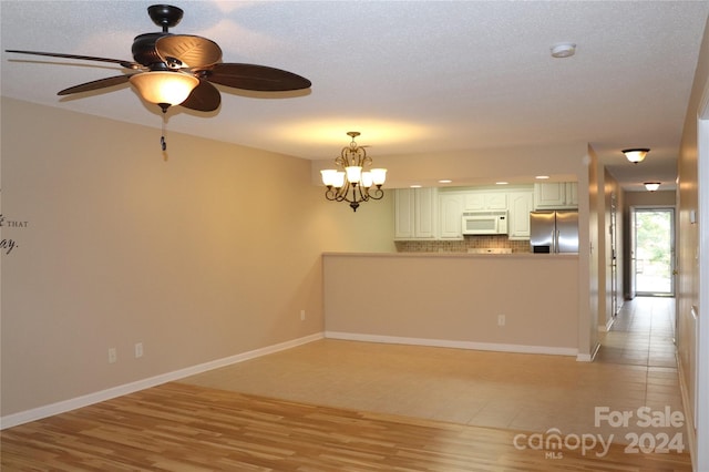 empty room featuring ceiling fan with notable chandelier, a textured ceiling, and light hardwood / wood-style flooring