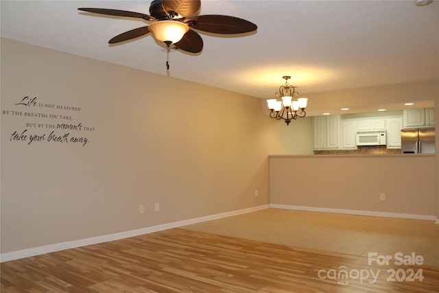 empty room featuring ceiling fan with notable chandelier and light hardwood / wood-style flooring