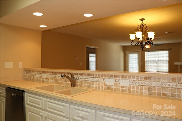 kitchen featuring pendant lighting, sink, stainless steel dishwasher, decorative backsplash, and a notable chandelier