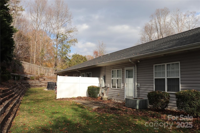 rear view of house featuring a yard, roof with shingles, and fence