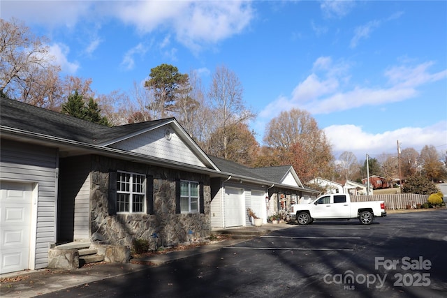 view of side of home with driveway, an attached garage, stone siding, and fence