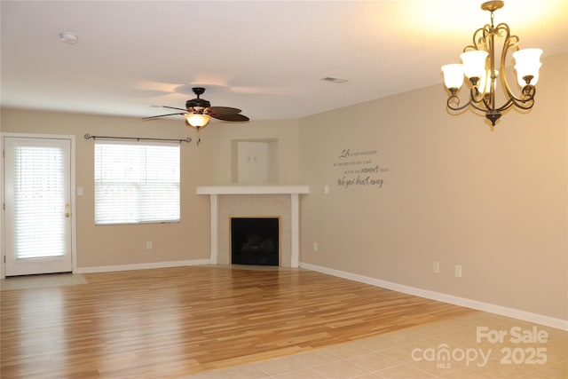 unfurnished living room with a fireplace, ceiling fan with notable chandelier, baseboards, and light wood finished floors