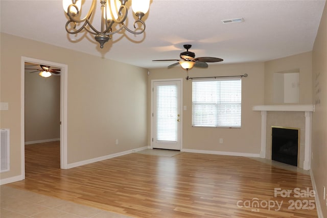 unfurnished living room with a tile fireplace, ceiling fan with notable chandelier, light wood finished floors, and visible vents