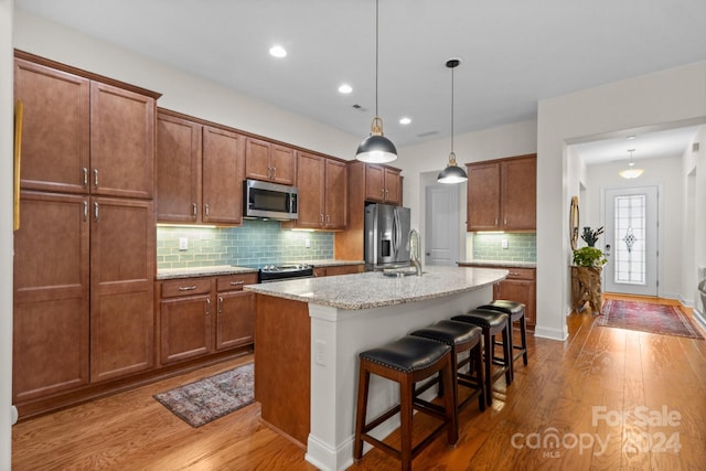 kitchen with light stone countertops, appliances with stainless steel finishes, a kitchen breakfast bar, light hardwood / wood-style floors, and an island with sink