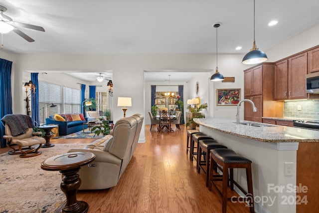 kitchen featuring light wood-type flooring, tasteful backsplash, light stone counters, ceiling fan, and decorative light fixtures