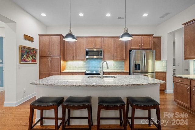 kitchen with sink, light stone counters, a kitchen island with sink, appliances with stainless steel finishes, and light wood-type flooring