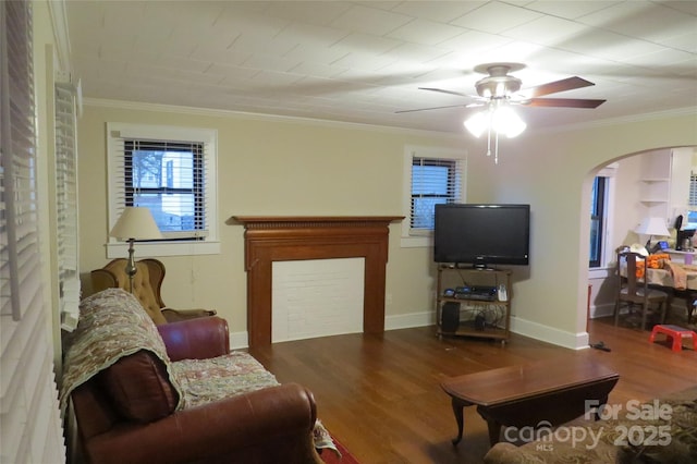 living area with arched walkways, crown molding, baseboards, and wood finished floors