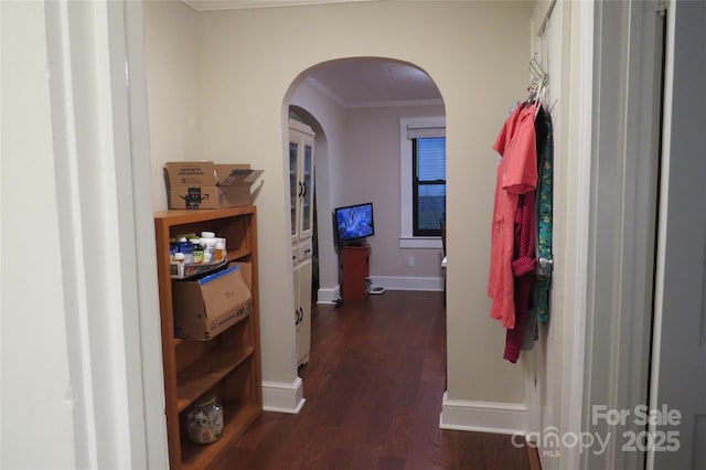 hall with dark wood-type flooring, arched walkways, crown molding, and baseboards