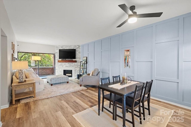 dining space with a stone fireplace, ceiling fan, and light wood-type flooring