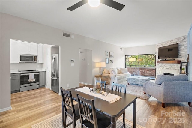 dining area with light wood-type flooring, a stone fireplace, and ceiling fan