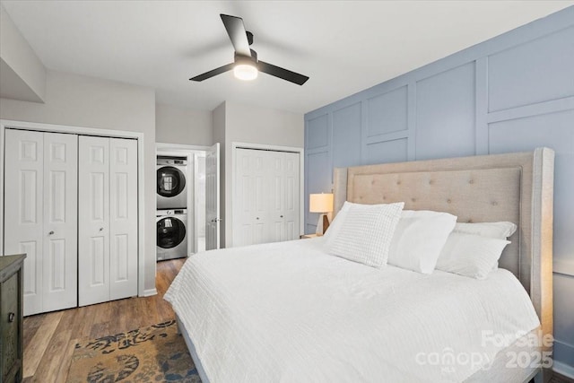 bedroom with ceiling fan, multiple closets, dark wood-type flooring, and stacked washer and clothes dryer