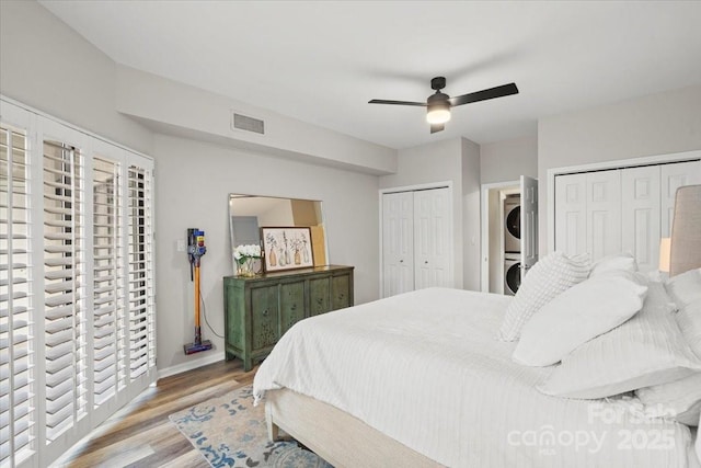 bedroom featuring ceiling fan, multiple closets, light hardwood / wood-style flooring, and stacked washer and clothes dryer