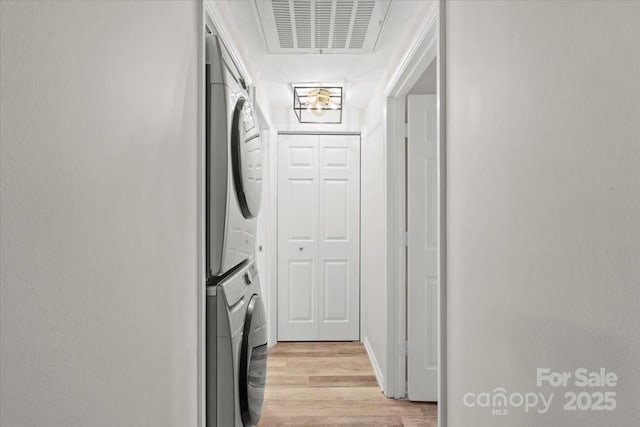 clothes washing area with stacked washer and dryer and light wood-type flooring