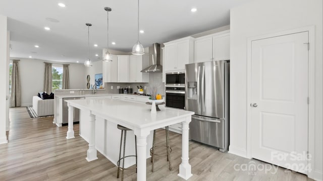 kitchen featuring a kitchen bar, appliances with stainless steel finishes, kitchen peninsula, wall chimney exhaust hood, and white cabinets