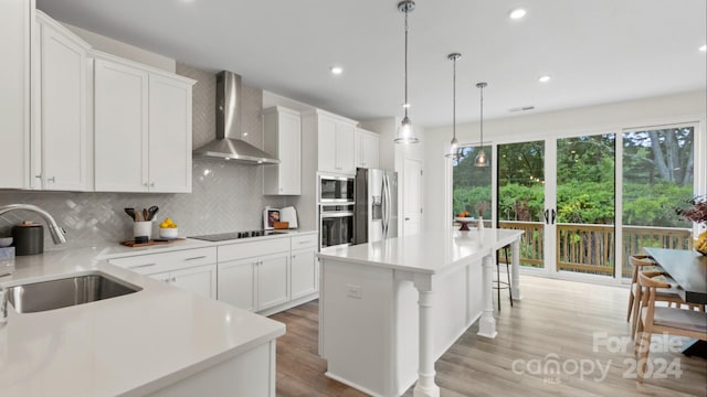 kitchen featuring appliances with stainless steel finishes, wall chimney exhaust hood, pendant lighting, white cabinets, and a kitchen island