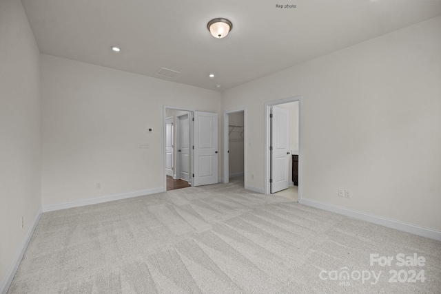 unfurnished bedroom featuring a walk in closet, a closet, and light colored carpet