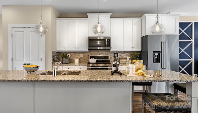 kitchen featuring pendant lighting, white cabinets, sink, light stone countertops, and appliances with stainless steel finishes