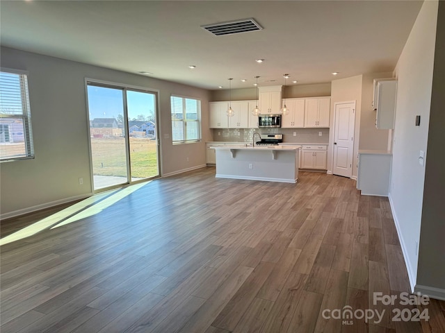 kitchen with white cabinets, light hardwood / wood-style floors, a kitchen island with sink, and appliances with stainless steel finishes