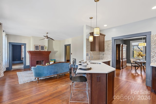 kitchen with sink, dark wood-type flooring, a brick fireplace, backsplash, and pendant lighting