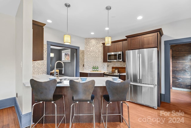 kitchen featuring sink, wood-type flooring, decorative light fixtures, decorative backsplash, and appliances with stainless steel finishes