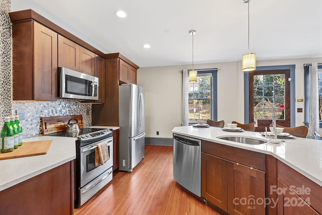 kitchen featuring backsplash, sink, light hardwood / wood-style flooring, decorative light fixtures, and stainless steel appliances