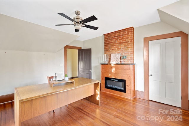 unfurnished office featuring ceiling fan, a fireplace, wood-type flooring, and vaulted ceiling