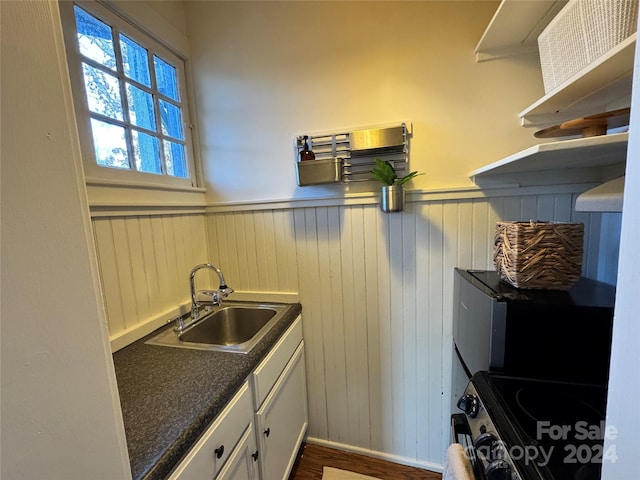 kitchen with dark wood-type flooring, sink, electric range, white cabinets, and wood walls