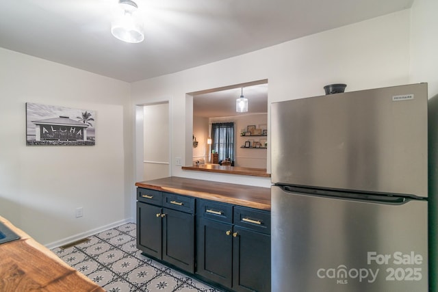 kitchen with blue cabinetry, pendant lighting, butcher block countertops, and stainless steel refrigerator