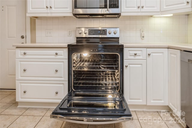 kitchen featuring backsplash, white cabinets, light tile patterned floors, and appliances with stainless steel finishes