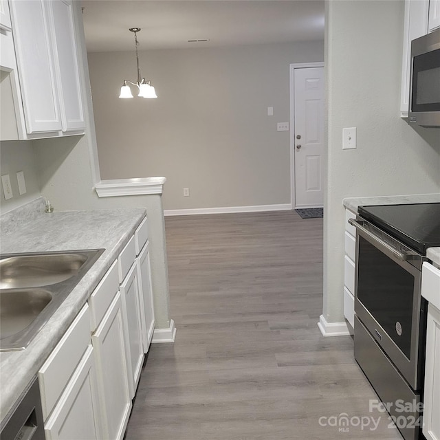 kitchen featuring white cabinetry, stainless steel appliances, decorative light fixtures, and light wood-type flooring