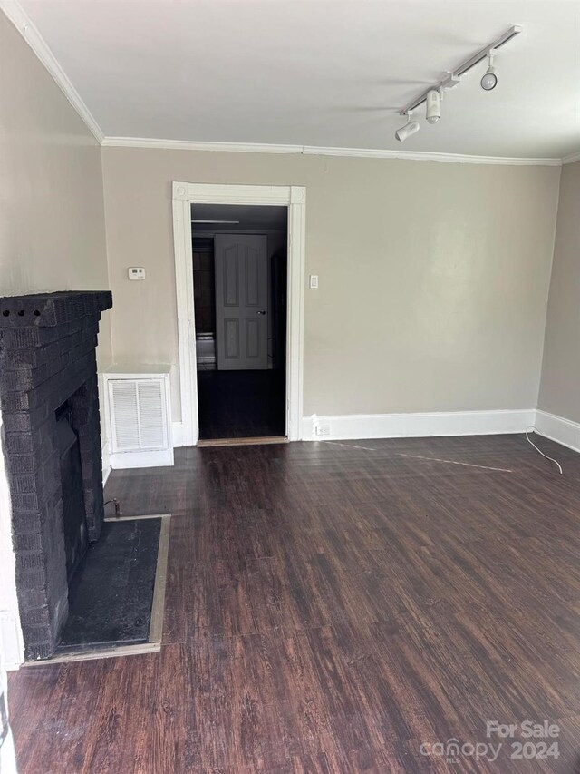 unfurnished living room with rail lighting, a fireplace, crown molding, and dark wood-type flooring