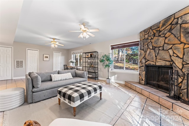 living room with a stone fireplace, ceiling fan, and light tile patterned floors