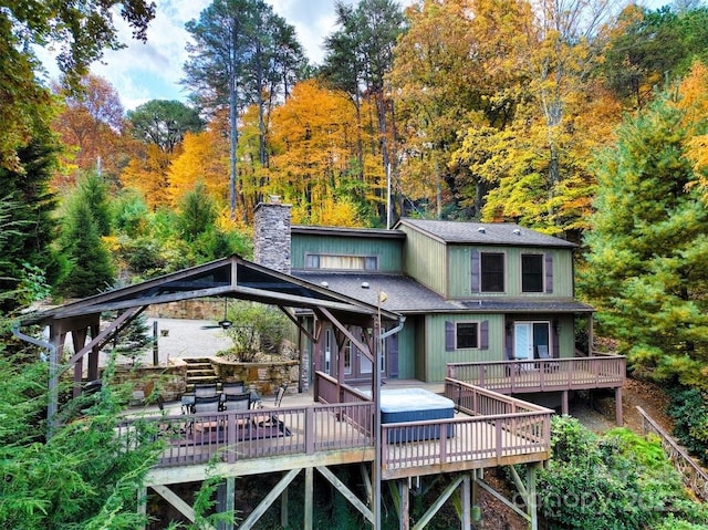 rear view of property featuring a deck, a view of trees, and a chimney