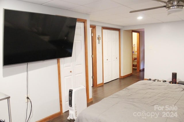 bedroom with a paneled ceiling, ceiling fan, dark hardwood / wood-style floors, and two closets