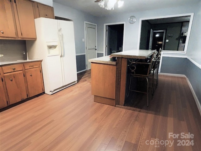 kitchen featuring ceiling fan, white refrigerator with ice dispenser, a kitchen bar, a kitchen island, and light wood-type flooring