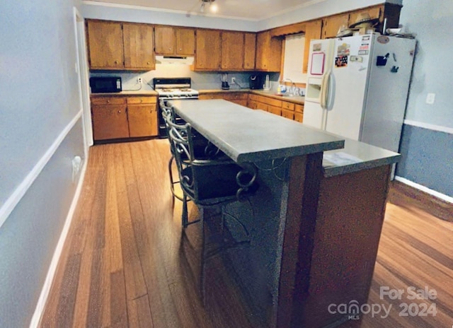 kitchen with a breakfast bar, white appliances, sink, a kitchen island, and light hardwood / wood-style floors