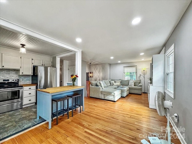 kitchen with white cabinets, a kitchen breakfast bar, light wood-type flooring, butcher block countertops, and stainless steel appliances