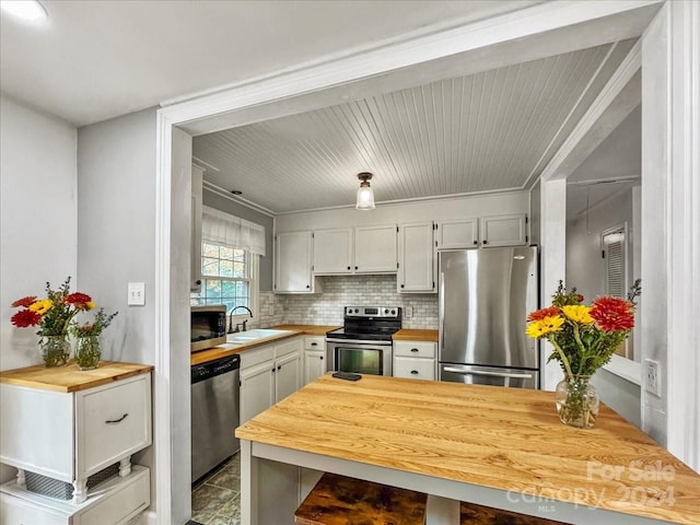 kitchen featuring tasteful backsplash, stainless steel appliances, crown molding, sink, and butcher block counters