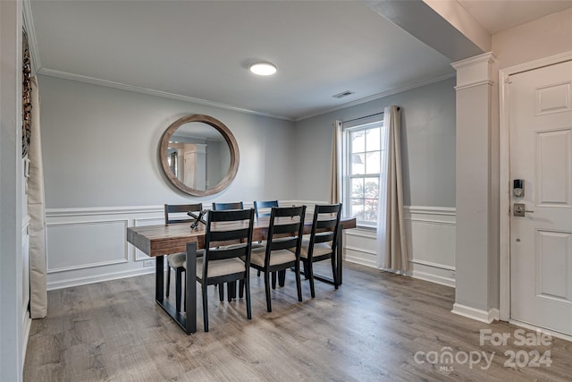 dining space with light wood-type flooring, crown molding, and ornate columns