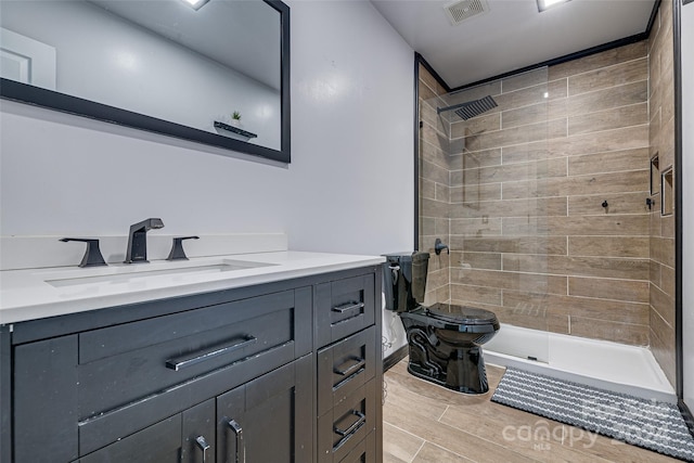 bathroom featuring hardwood / wood-style floors, vanity, toilet, and a tile shower