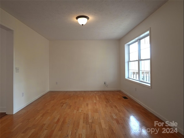 spare room featuring a textured ceiling and light hardwood / wood-style floors