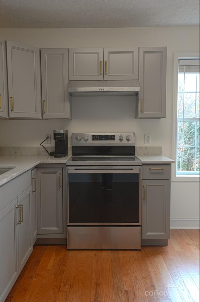 kitchen featuring electric range, gray cabinets, light stone counters, and light hardwood / wood-style flooring