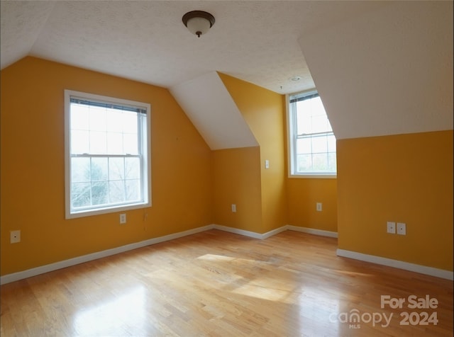 additional living space with a textured ceiling, vaulted ceiling, and light hardwood / wood-style flooring