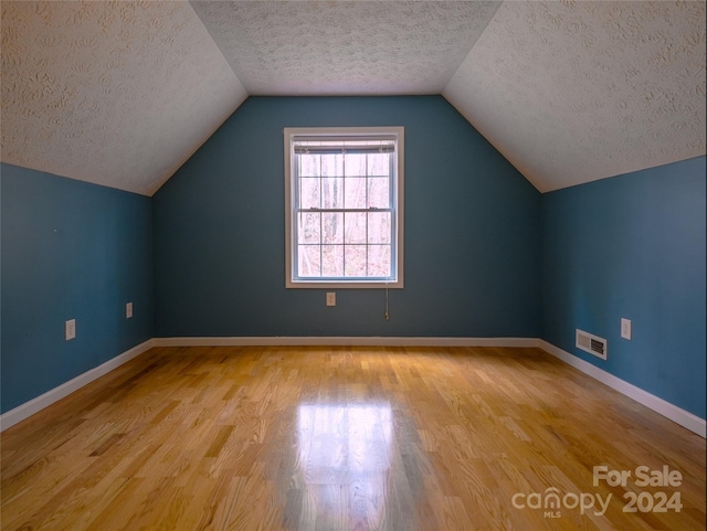 additional living space with a textured ceiling, light hardwood / wood-style floors, and vaulted ceiling