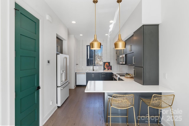 kitchen featuring kitchen peninsula, hanging light fixtures, sink, white appliances, and a kitchen bar