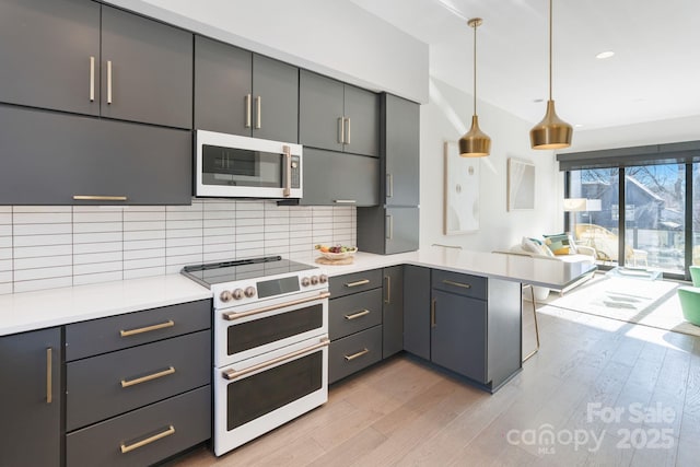 kitchen featuring white appliances, light hardwood / wood-style floors, kitchen peninsula, hanging light fixtures, and tasteful backsplash